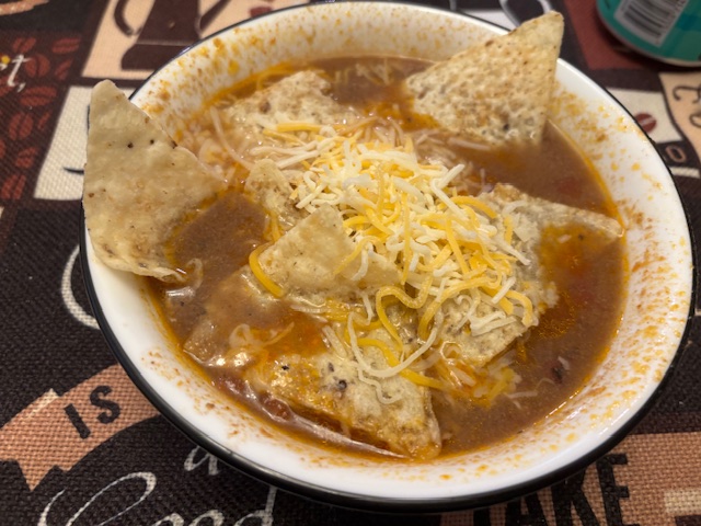 taco soup garnished with tortilla chips and cheese in a white soup bowl.